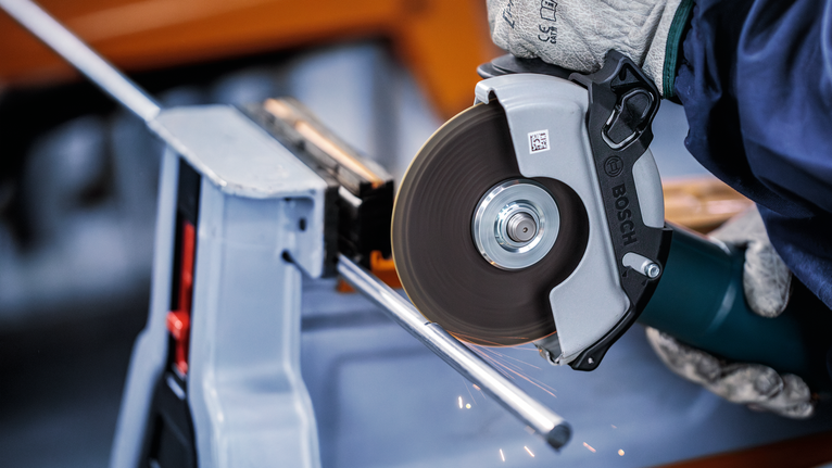 Person wearing safety equipment cuts a metal rod with an angle grinder.