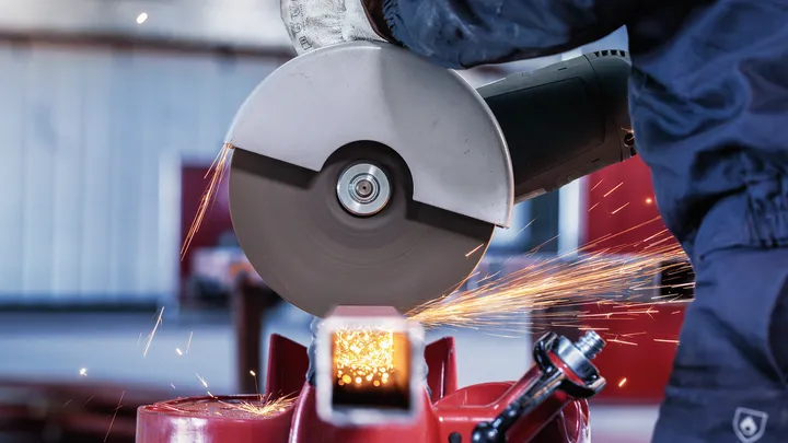 Person wearing safety equipment cutting metal with a large circular saw, sparks flying.
