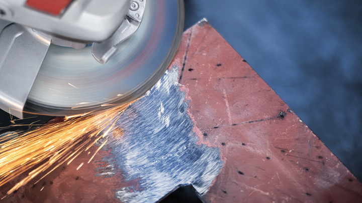 Angle grinder producing sparks while sanding the edge of a metal sheet.