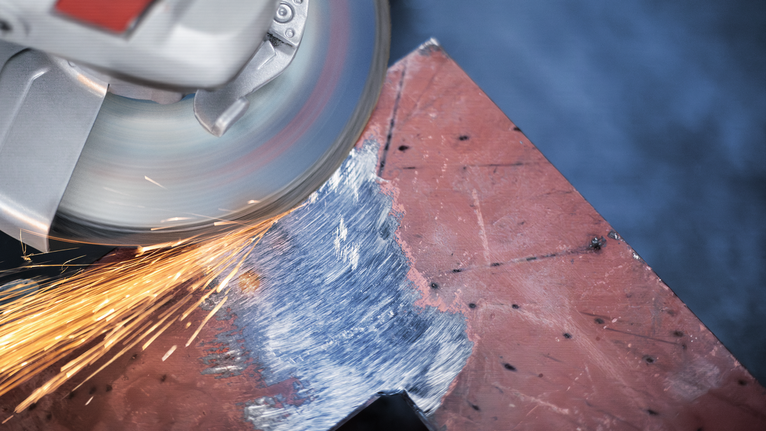 Angle grinder producing sparks while sanding the edge of a metal sheet.
