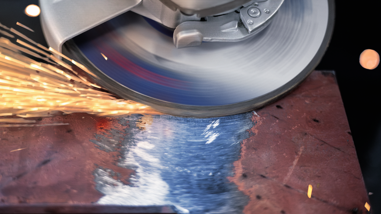 A cutting disc grinds a metal sheet, producing bright sparks.