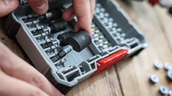 Person selecting a socket from a tool kit on a wooden workbench.