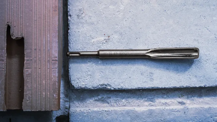 Chisel drill bit placed on a concrete block surface.