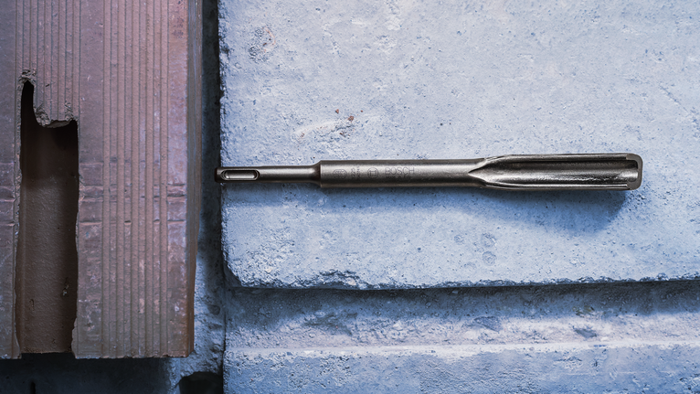 Chisel drill bit placed on a concrete block surface.