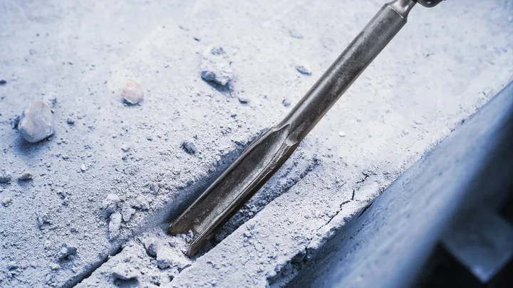 Chisel attachment breaking a straight groove into a concrete surface.