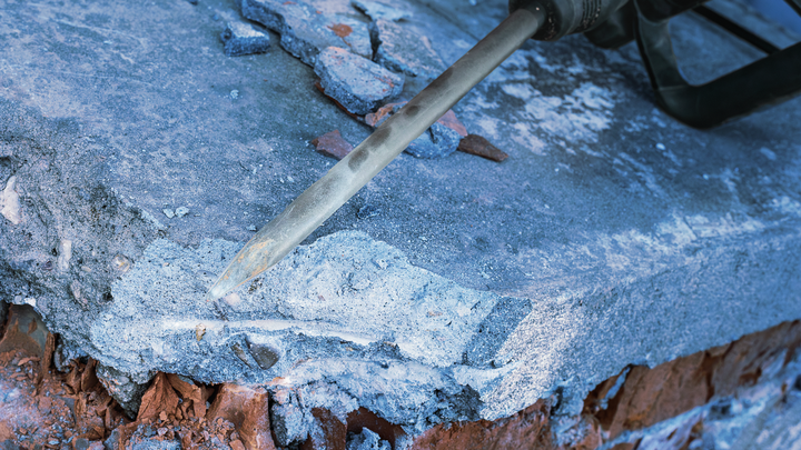 A demolition hammer breaks concrete along the edge of a brick structure.