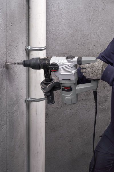 A person wearing safety equipment drills into a concrete wall with a rotary hammer.