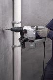 A person wearing safety equipment drills into a concrete wall with a rotary hammer.