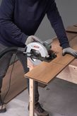 A person wearing safety equipment uses a circular saw to cut wooden flooring.