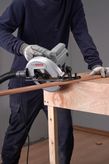 A person wearing safety equipment uses a circular saw to cut a wooden board.