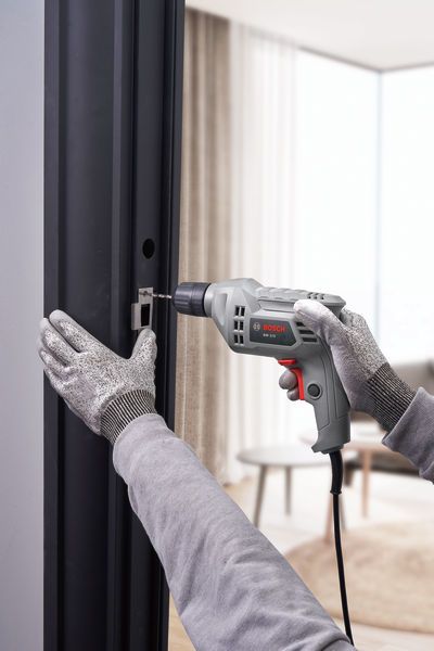 A person wearing safety equipment drills into a metal door frame.