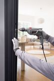 A person wearing safety equipment drills into a door frame with a power drill.