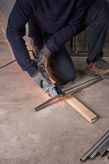 A person wearing safety equipment cuts a metal pipe with a grinder on a concrete floor.