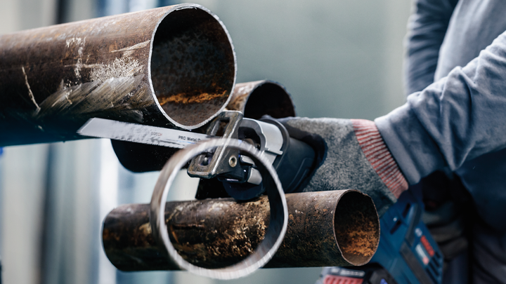 Person wearing safety equipment cuts a metal pipe with a reciprocating saw.
