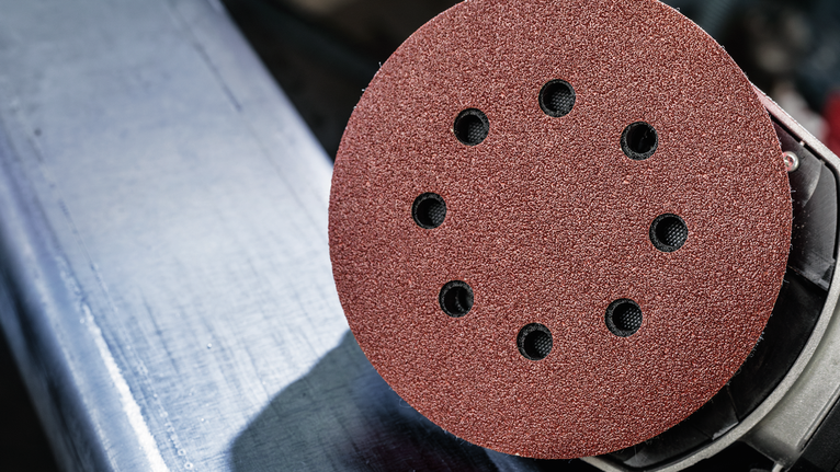 Orbital sander with a red abrasive disc rests on a metal surface.