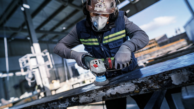 Person wearing safety equipment polishes a large metal surface with a power sander.