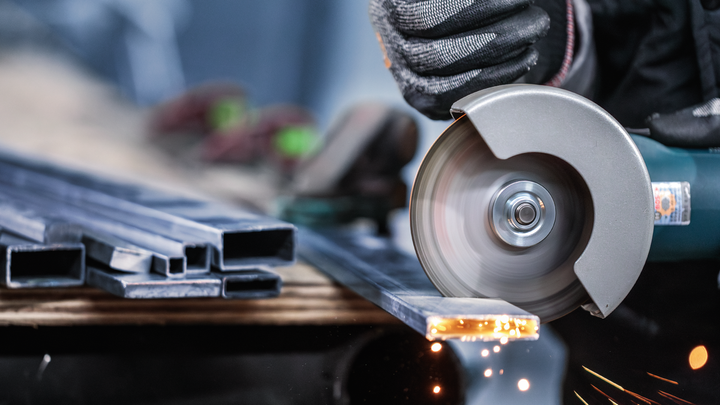 A person wearing safety equipment cuts metal profiles with an angle grinder.