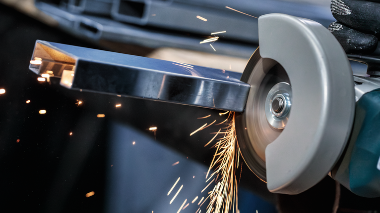 Person wearing safety equipment grinds a metal bar with a handheld cutting tool.