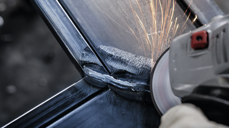 Person wearing safety equipment grinds a metal weld, creating sparks.