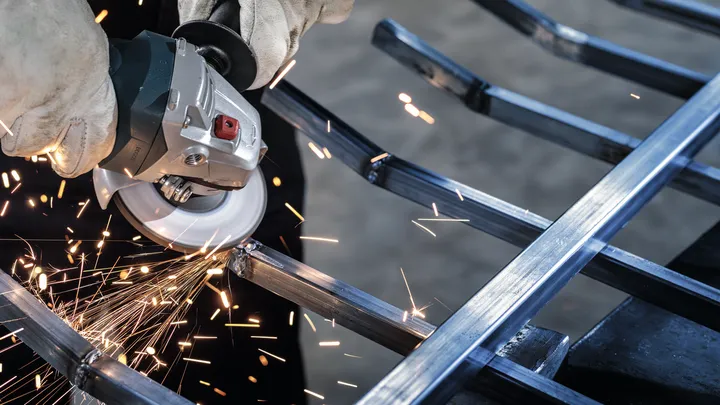 Person wearing safety equipment grinds a metal frame, creating sparks.