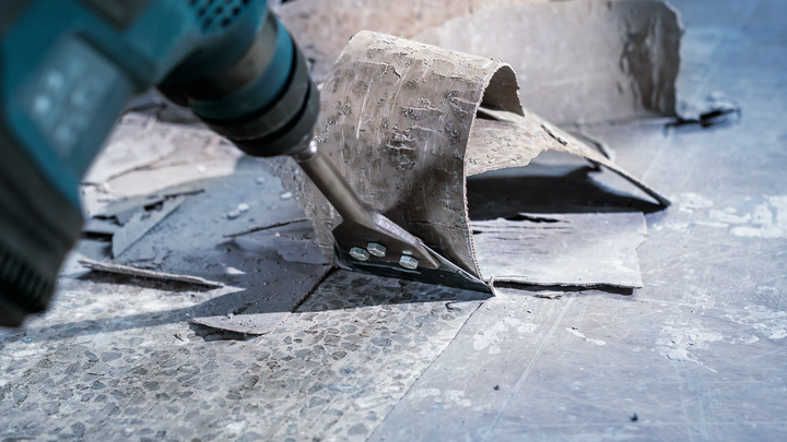 Power tool scraper attachment removing old flooring from a concrete surface.