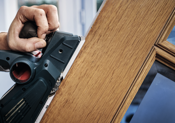 Person planing the edge of a wooden door indoors.