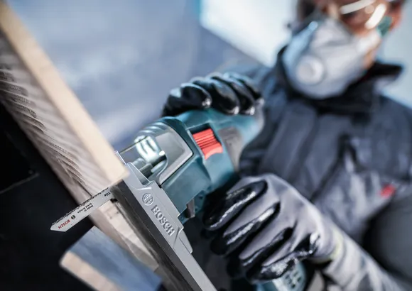 Person wearing safety equipment uses a reciprocating saw to cut wood.