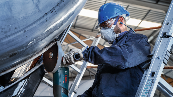 Person wearing safety equipment uses an angle grinder to cut metal.