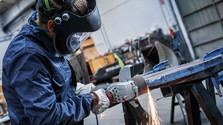 A person wearing safety equipment grinds a large metal surface, creating sparks.