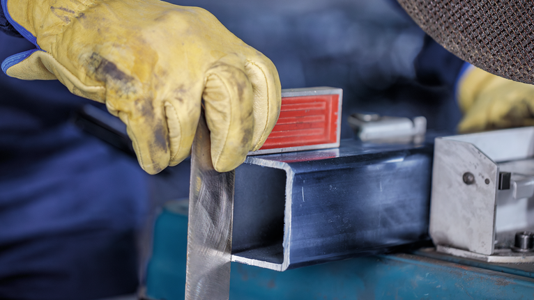 Worker wearing safety equipment holds a metal piece near a cutting machine.