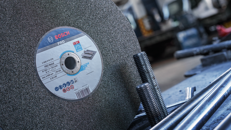 Large abrasive cutting disc positioned next to threaded metal rods in a workshop.