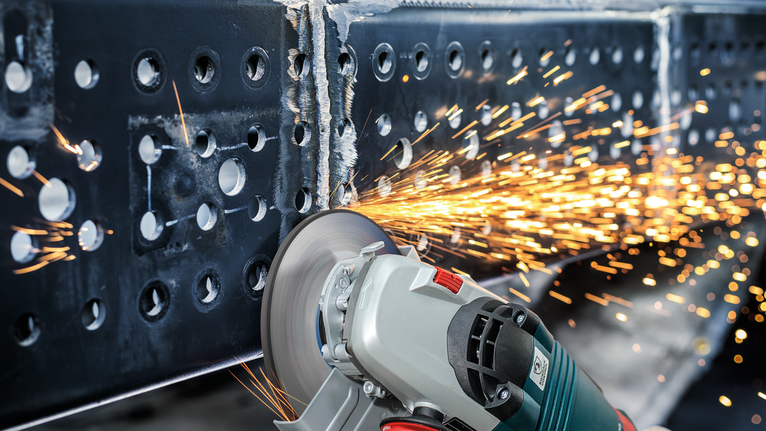 Angle grinder cutting through a metal beam as sparks fly.