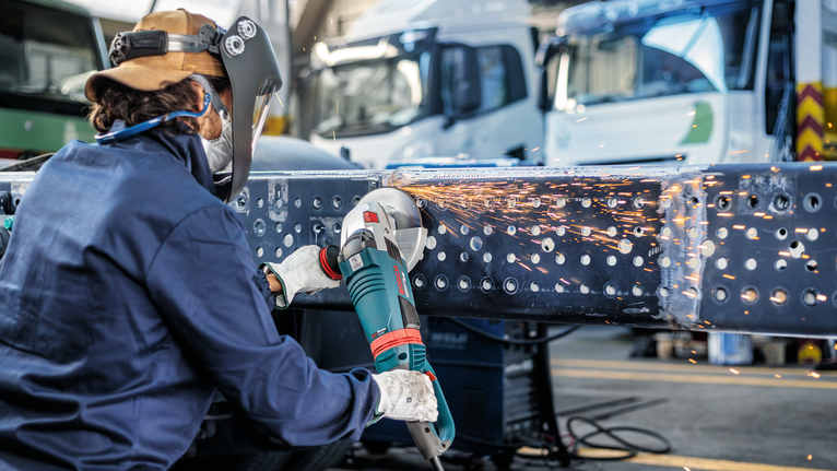 Person wearing safety equipment grinds metal beams, creating sparks.