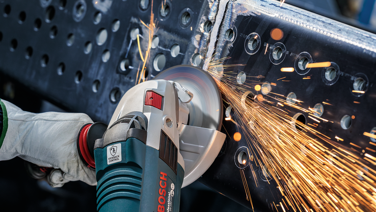 Person wearing safety equipment grinds a metal beam, producing sparks.