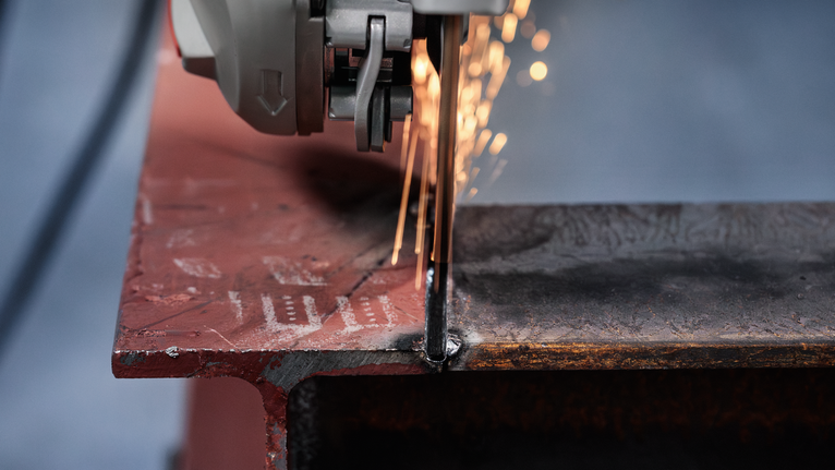 Cutting tool slicing through a steel beam, producing bright sparks.