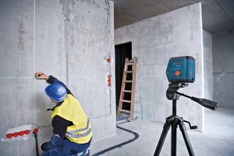 A person wearing safety equipment marks a wall using a laser leveling tool.