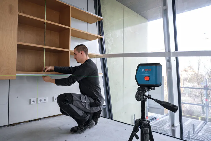A person aligns a shelf using a laser leveling tool in a modern room.