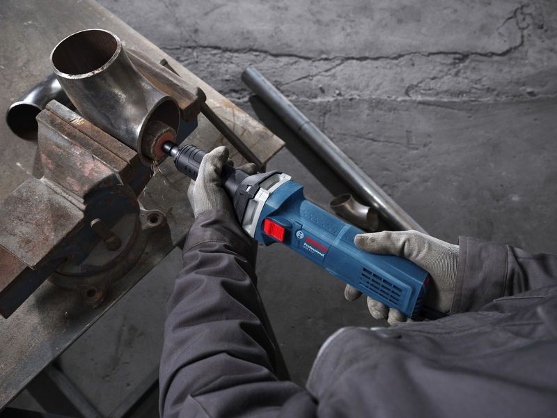 A person wearing safety equipment grinds the inside of a metal pipe with a straight grinder.