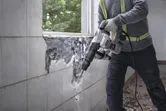 A person wearing safety equipment uses a demolition breaker to remove wall tiles.