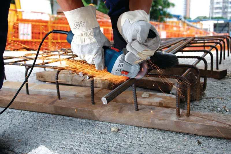 A person wearing safety equipment uses an angle grinder to cut rebar on a construction site.