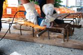 A person wearing safety equipment uses an angle grinder to cut rebar on a construction site.