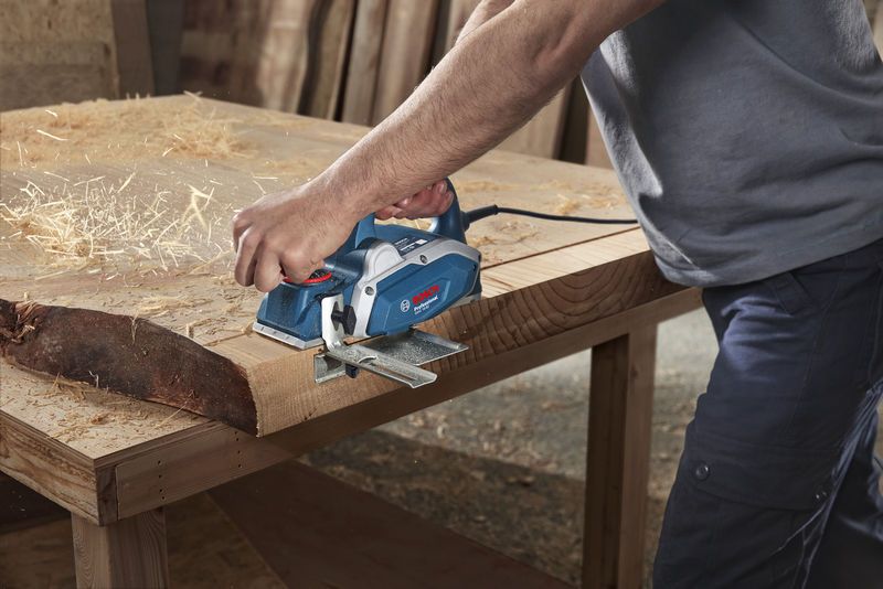 A person uses an electric planer to smooth a wooden plank on a workbench.