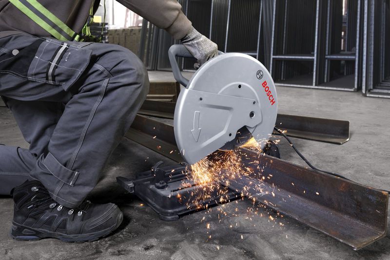 A person wearing safety equipment operates a chop saw cutting a steel beam.