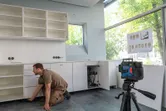 Person installing kitchen cabinets uses a laser leveling tool on a tripod for alignment.