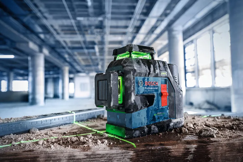 Laser leveling tool projecting green lines on a dusty floor at a construction site.