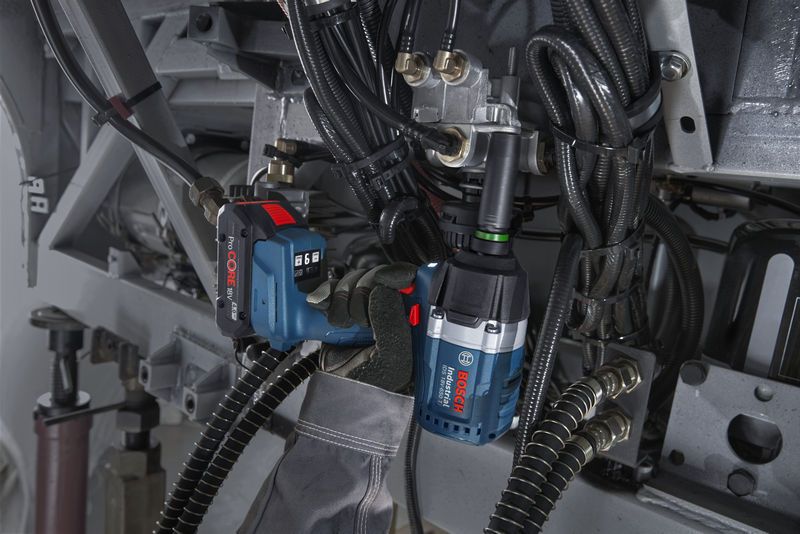 A person wearing safety equipment uses an impact wrench to tighten bolts on machinery.