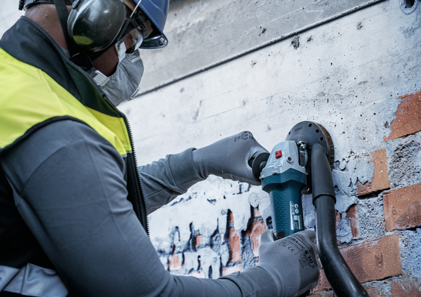 Person wearing safety equipment grinds paint from a brick wall with a power tool.