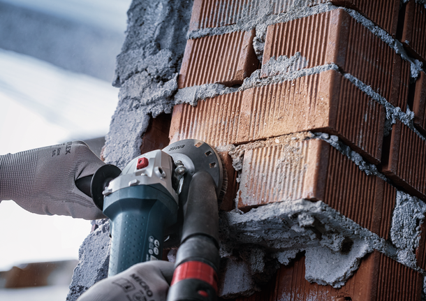 Person wearing safety equipment grinds grooves into a brick wall using a power tool.