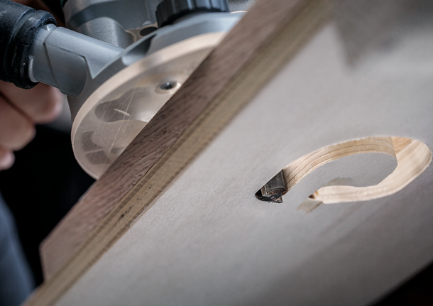 Person operates a router to carve a curved groove in a wooden board.
