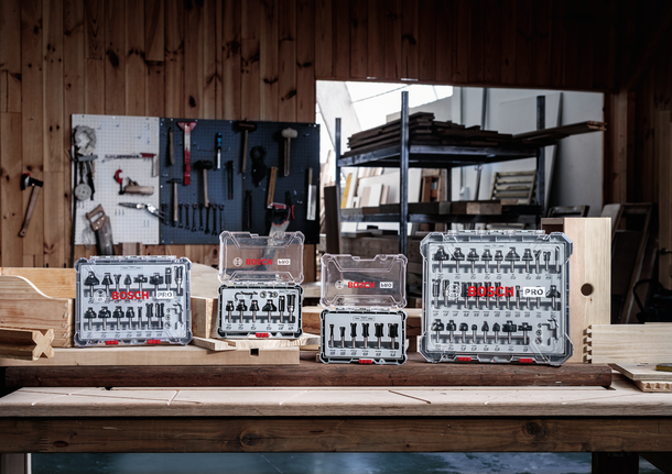 Four router bit sets displayed on a wooden workbench in a carpentry workshop.